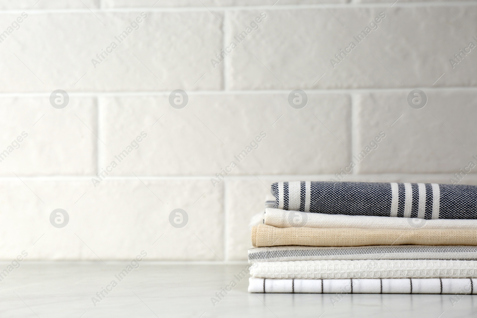 Photo of Stack of soft kitchen towels on table near white brick wall, space for text