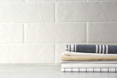 Stack of soft kitchen towels on table near white brick wall, space for text