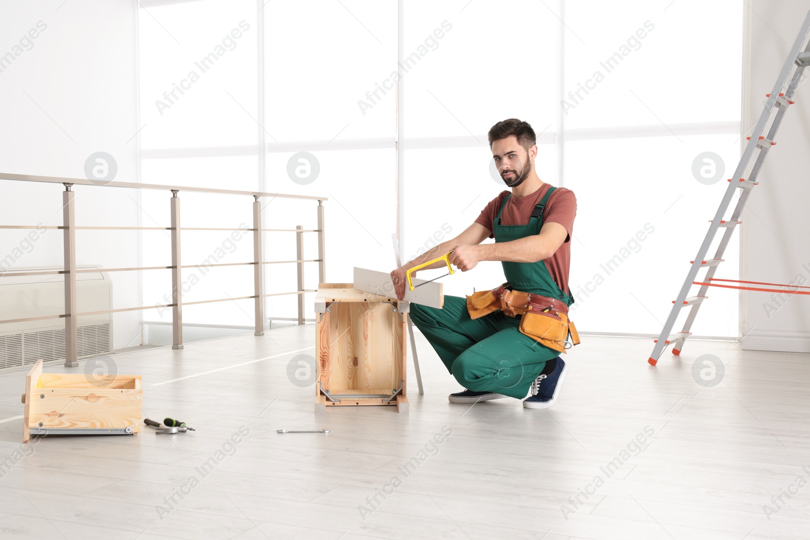 Photo of Carpenter in uniform making furniture indoors. Professional construction tools