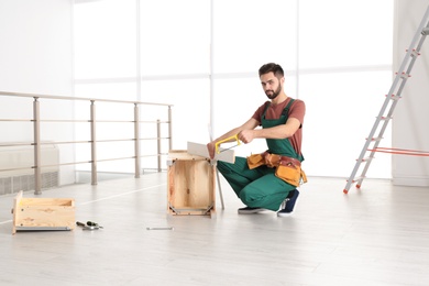 Carpenter in uniform making furniture indoors. Professional construction tools