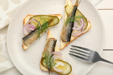Photo of Delicious sandwiches with sprats, pickled cucumber, onion and dill served on white wooden table, top view