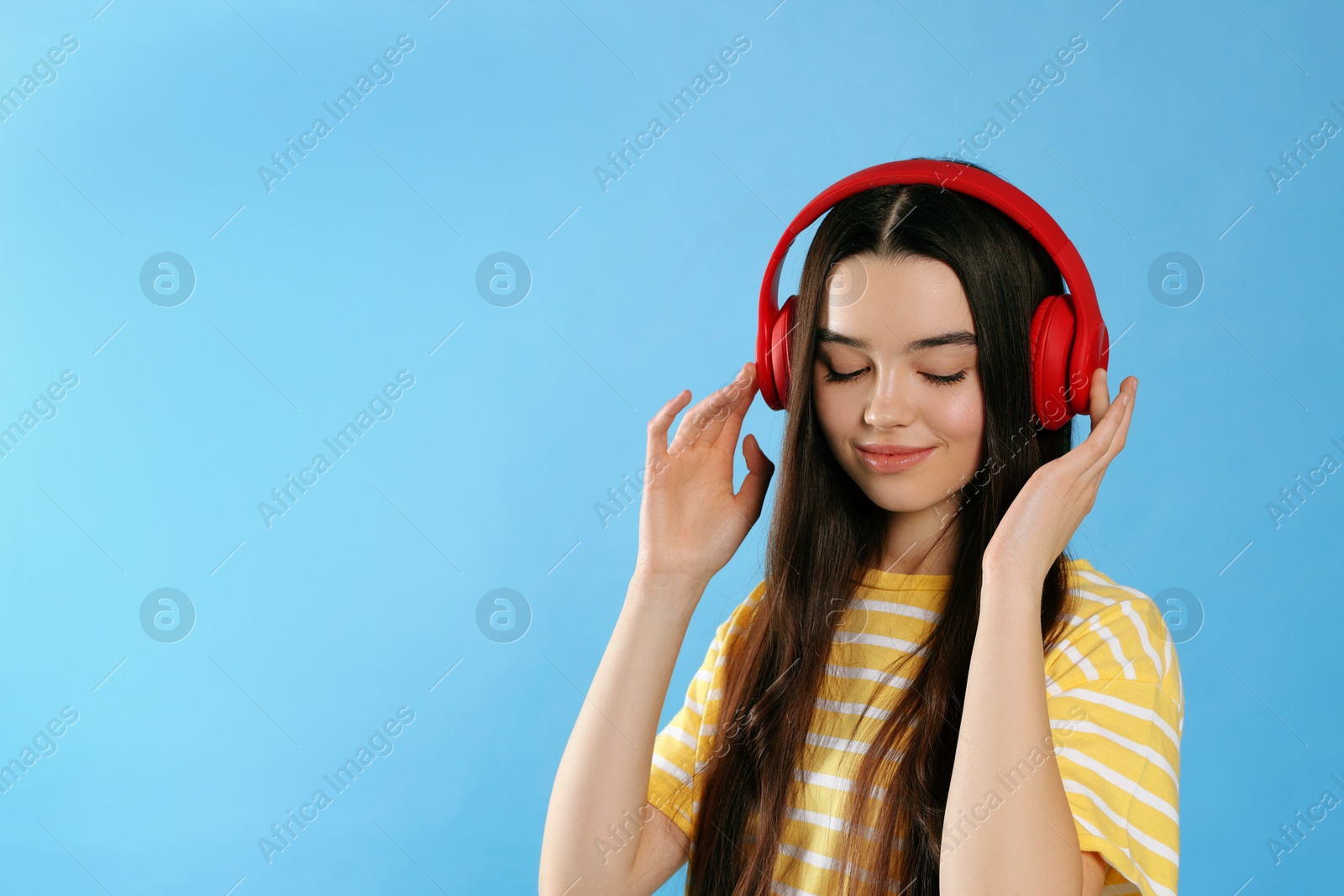 Photo of Teenage girl listening music with headphones on light blue background. Space for text