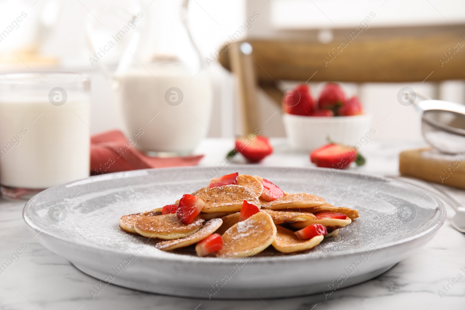 Photo of Delicious mini pancakes cereal with strawberries served on white marble table