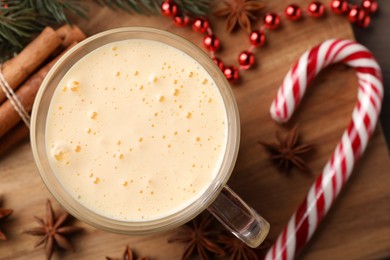 Photo of Glass of delicious eggnog, candy cane and anise stars on wooden table, flat lay