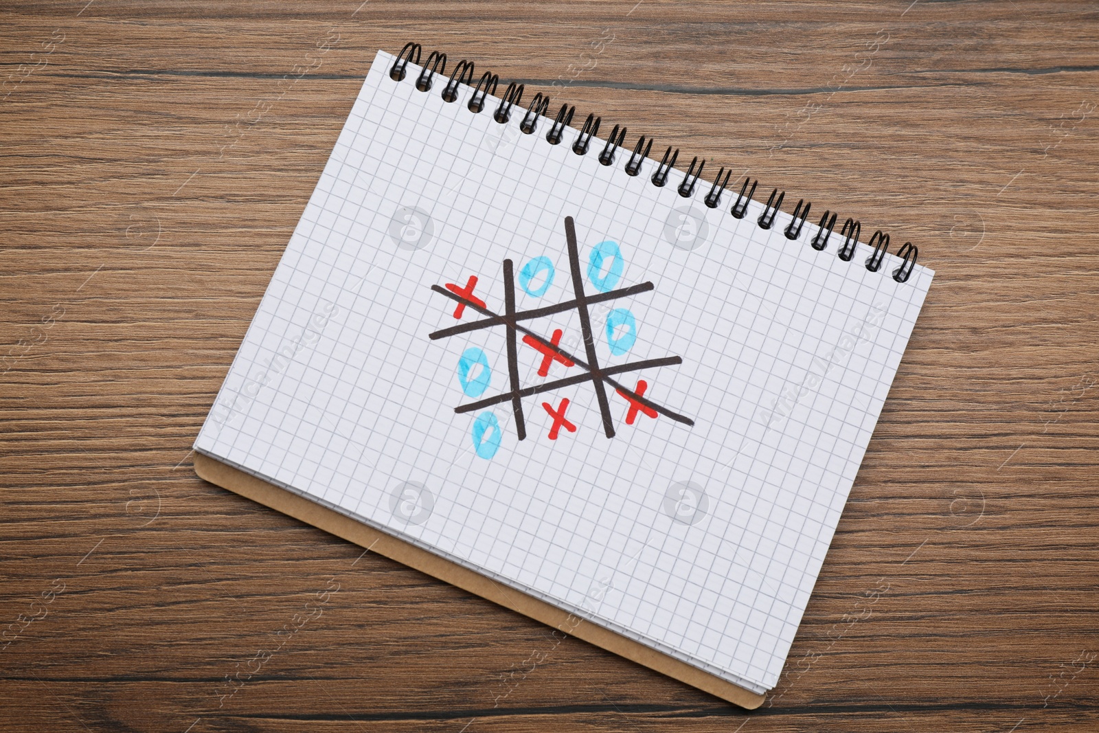 Photo of Notebook with tic tac toe game on wooden table, top view