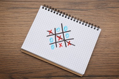 Photo of Notebook with tic tac toe game on wooden table, top view