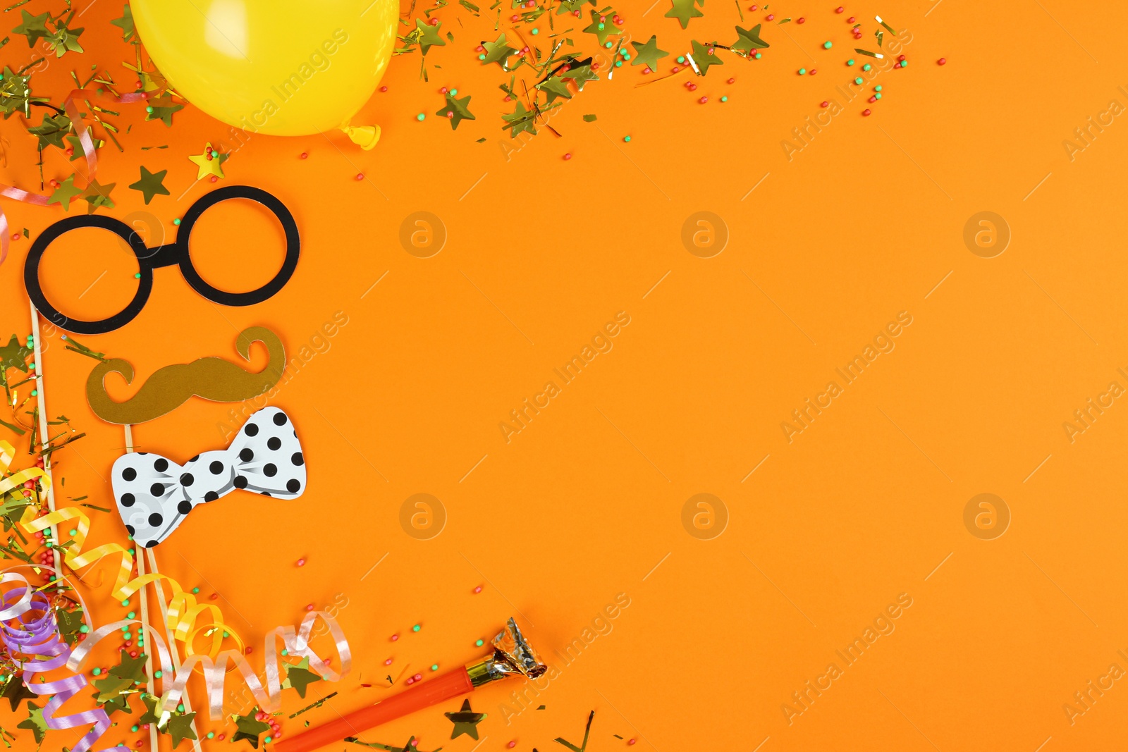 Photo of Colorful serpentine streamers and other party accessories on orange background, flat lay. Space for text