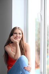 Young happy woman sitting near window at home