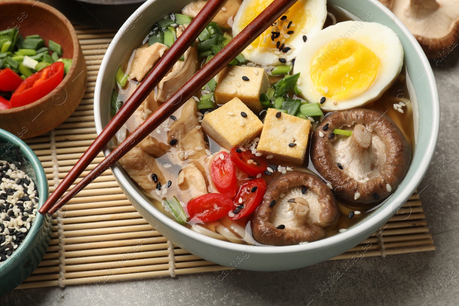 Photo of Bowl of delicious ramen and ingredients on grey table, closeup. Noodle soup