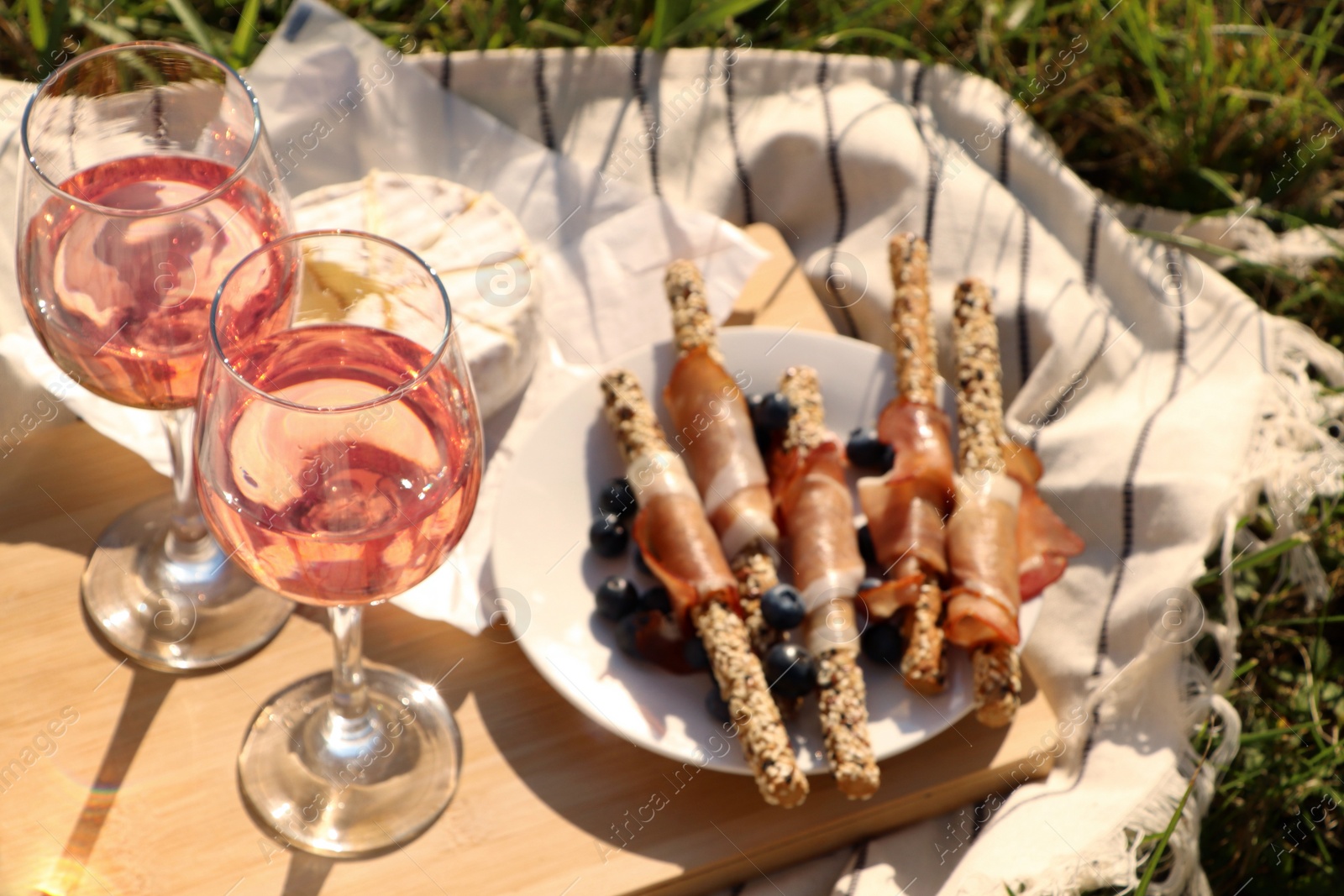 Photo of Glasses of delicious rose wine and food on picnic blanket outdoors