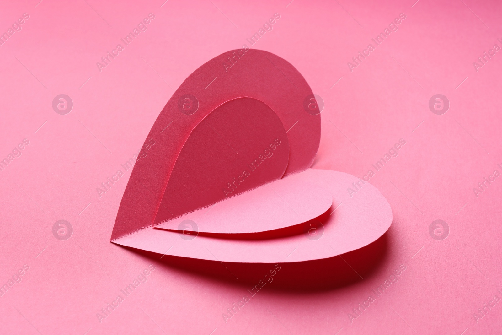 Photo of Two paper hearts on pink background, closeup