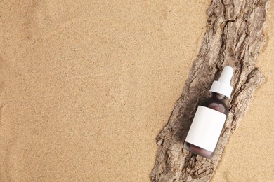 Bottle with serum and bark on sand, top view with space for text. Cosmetic product