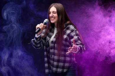 Emotional woman with microphone singing on stage in color lighted smoke