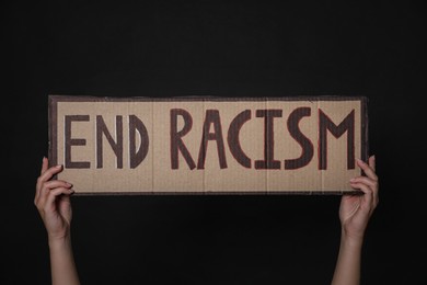 Woman holding sign with phrase End Racism on black background, closeup