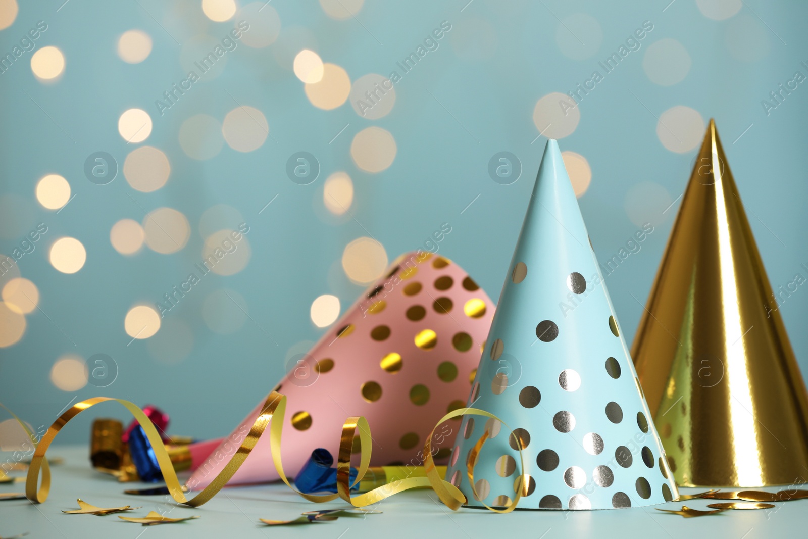 Photo of Party hats and festive items on table against blue background with blurred lights. Space for text