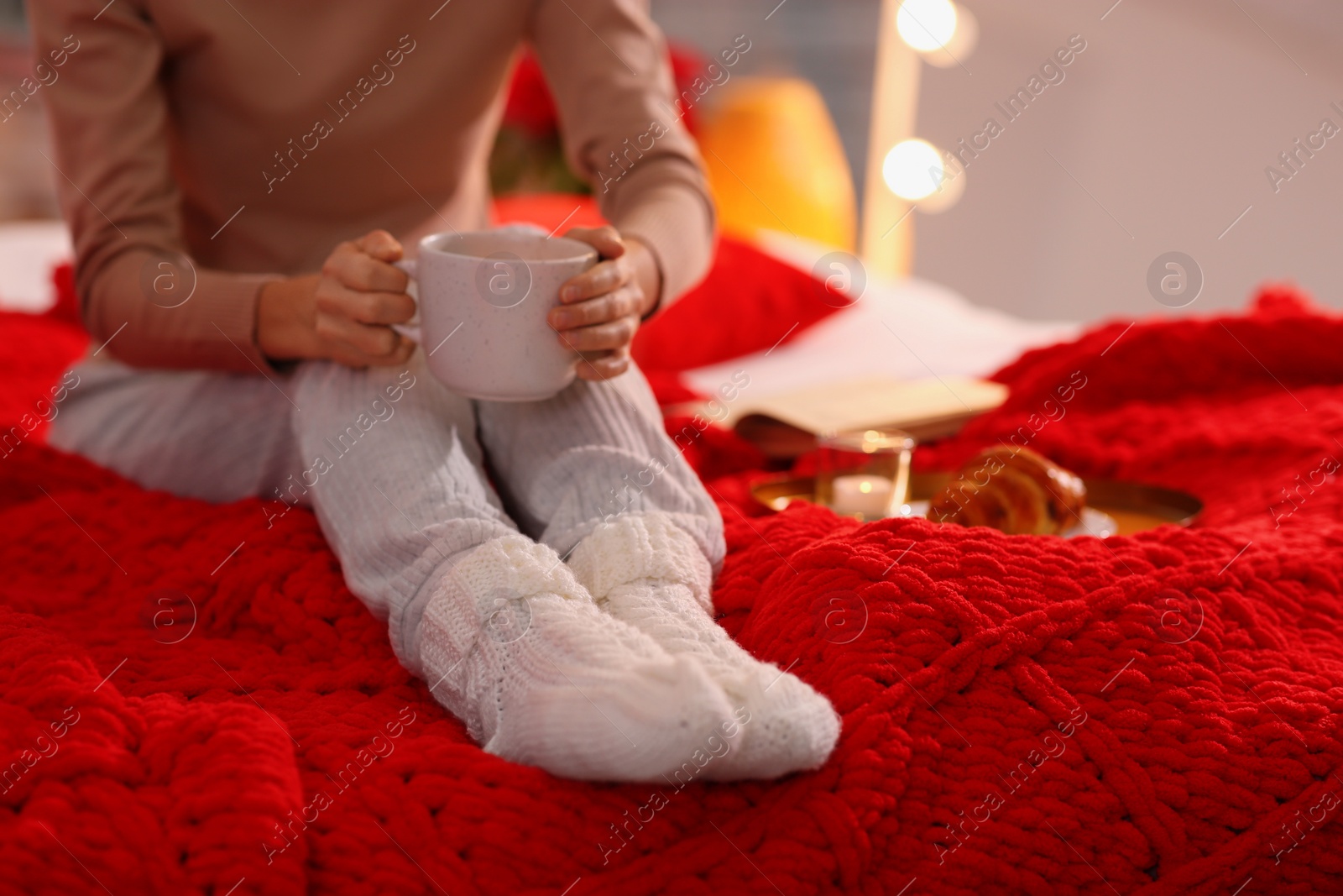 Photo of Woman with cup of drink relaxing on bed at home, closeup. Cozy atmosphere