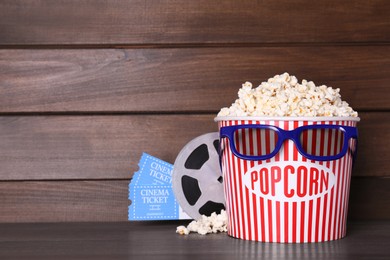 Photo of Delicious popcorn, 3D glasses, movie reel and tickets on wooden table. Space for text