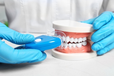 Photo of Dentist showing how to use teeth whitening device with educational model of oral cavity at table, closeup