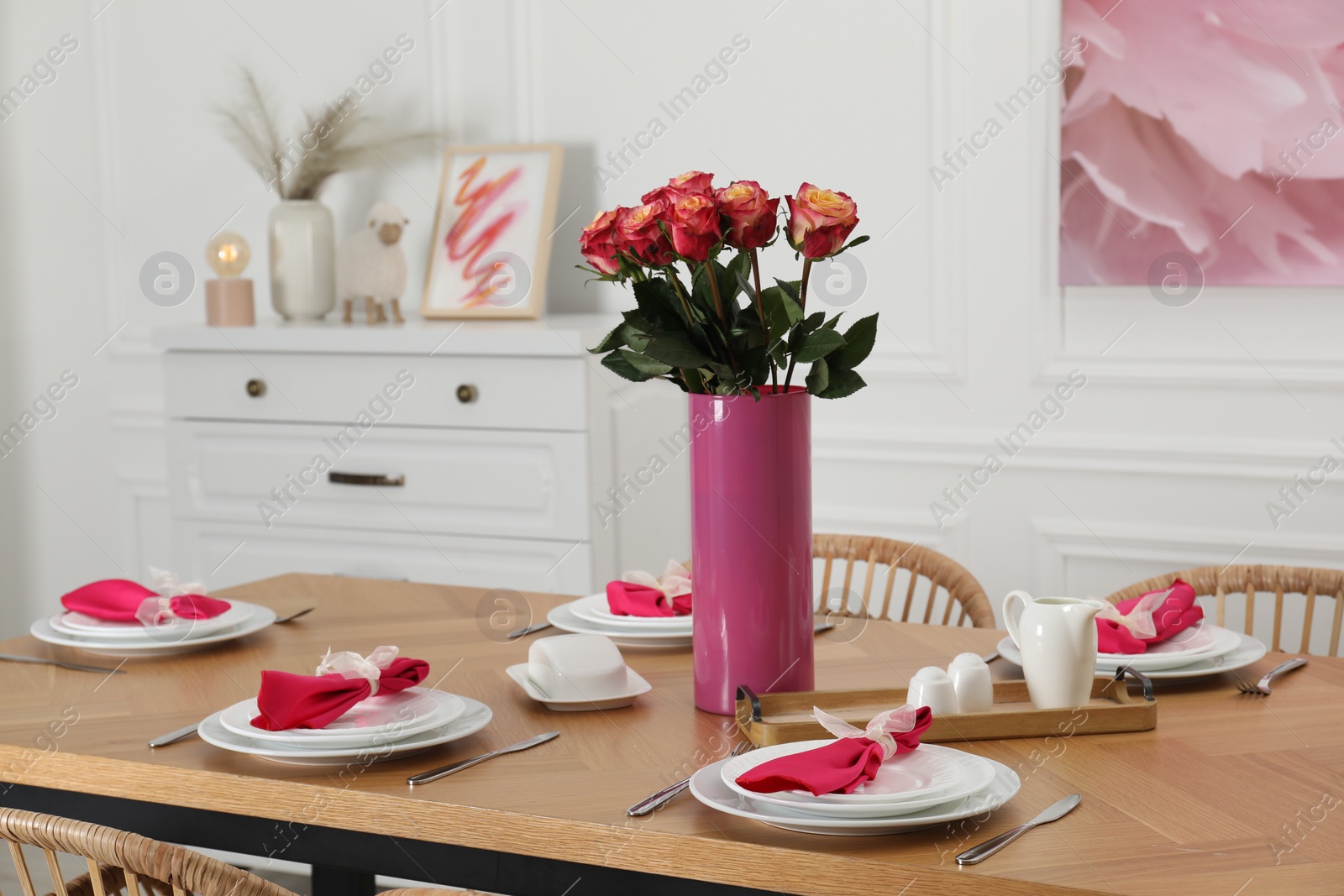 Photo of Color accent table setting. Plates, cutlery, pink napkins and vase with beautiful roses in dining room