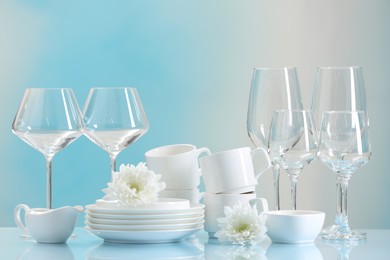 Set of many clean dishware, flowers and glasses on light blue table