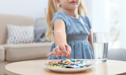 Photo of Little child taking pill from plate at home. Household danger