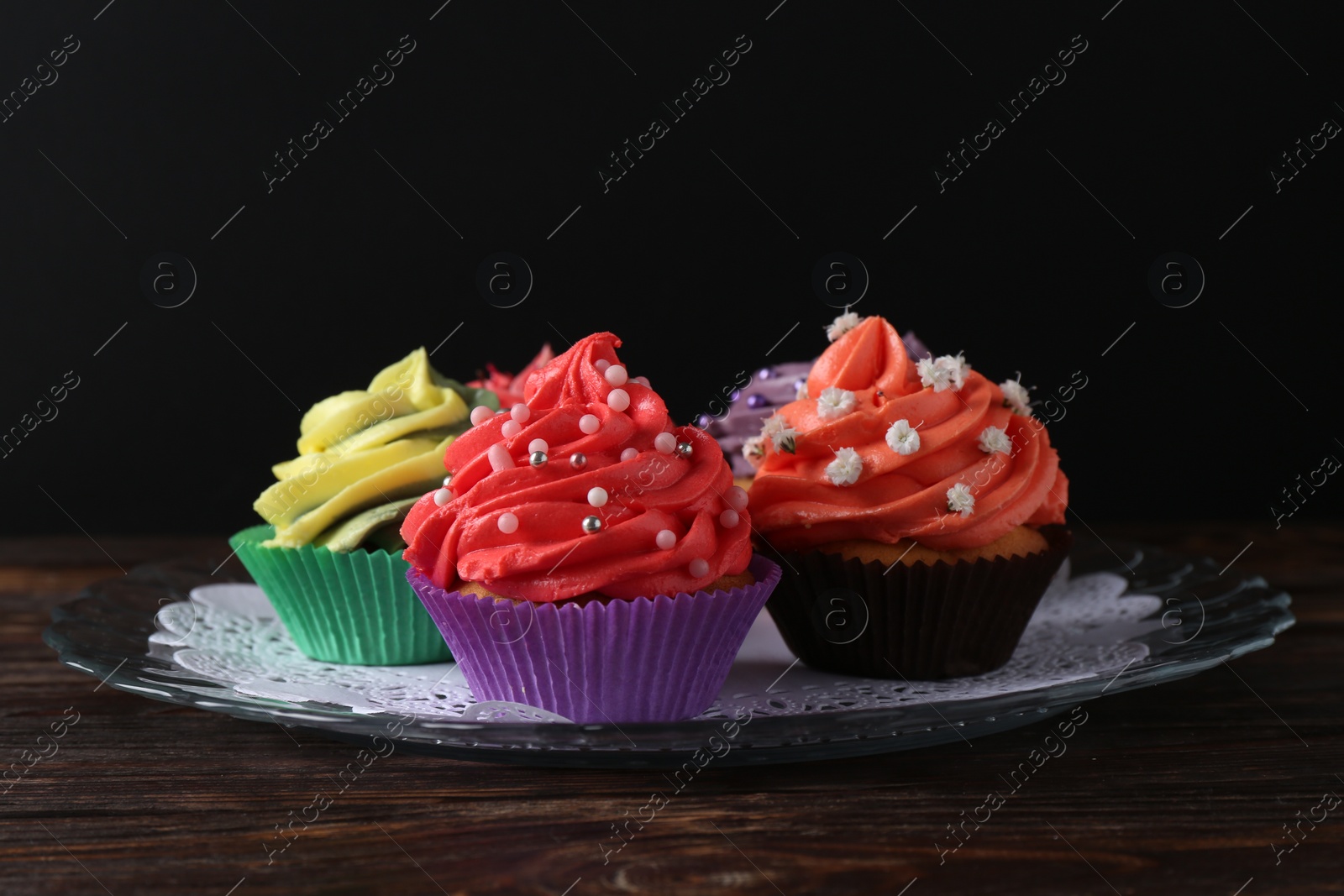 Photo of Delicious cupcake with bright cream on wooden table against black background