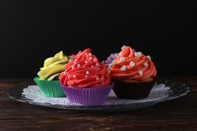 Photo of Delicious cupcake with bright cream on wooden table against black background