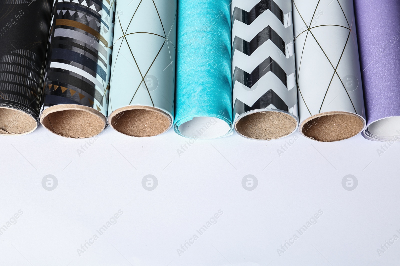 Photo of Rolls of festive wrapping paper and space for text on white background, closeup. Gift box packaging ideas