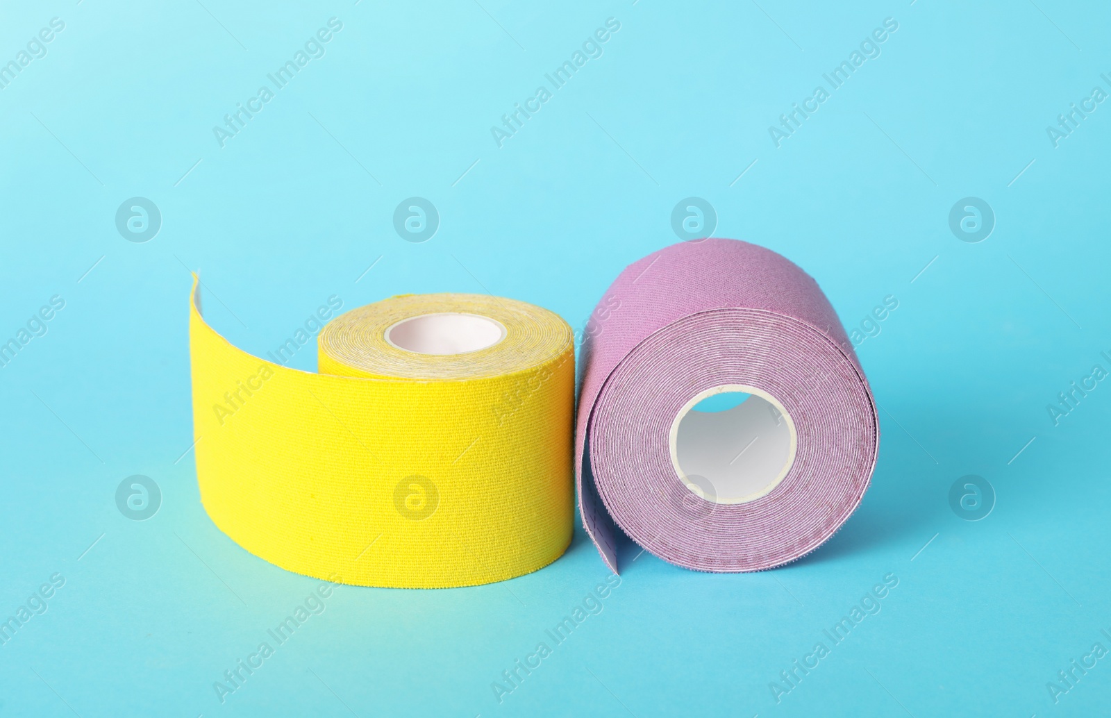 Photo of Bright kinesio tape in rolls on light blue background