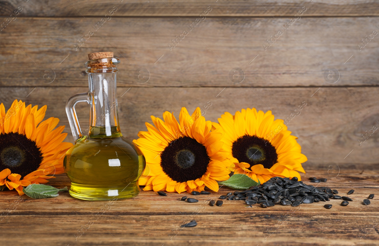 Photo of Sunflower cooking oil, seeds and yellow flowers on wooden table, space for text