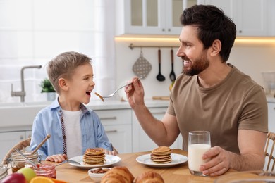 Father and his cute little son having breakfast at table in kitchen