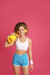 Photo of Beautiful African American woman with yoga mat and headphones on pink background