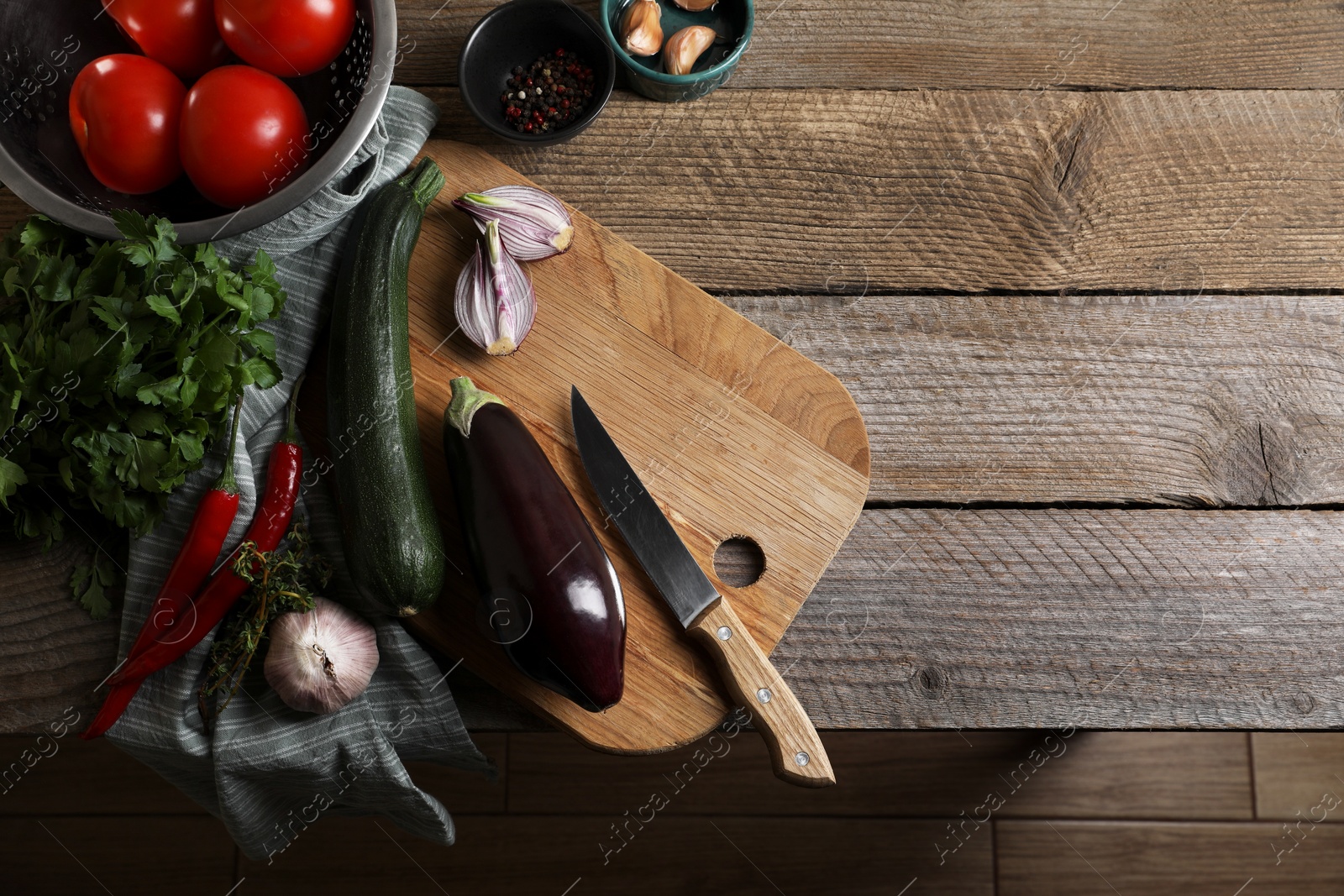 Photo of Cooking ratatouille. Vegetables, peppercorns, herbs and knife on wooden table, flat lay with space for text