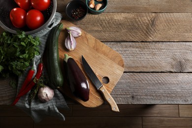 Photo of Cooking ratatouille. Vegetables, peppercorns, herbs and knife on wooden table, flat lay with space for text