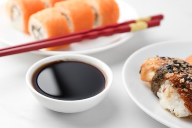 Photo of Bowl with tasty soy sauce, chopsticks and different types of sushi on white table, closeup