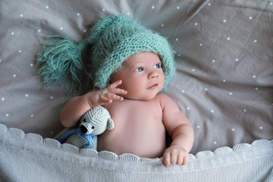Cute newborn baby in warm hat with toy lying on bed, top view
