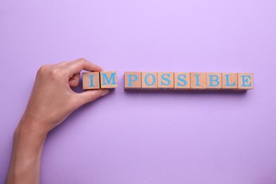 Photo of Motivation concept. Woman changing word from Impossible into Possible by removing wooden cubes on violet background, top view