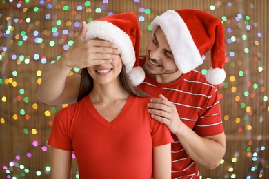 Photo of Young couple in Santa hats on blurred lights background. Christmas celebration