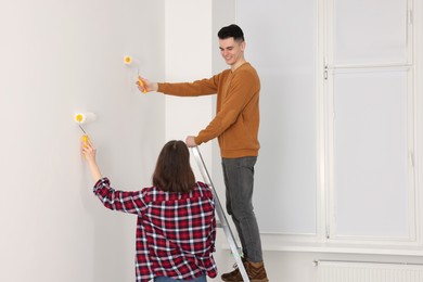 Photo of Young couple painting wall with rollers indoors. Room renovation