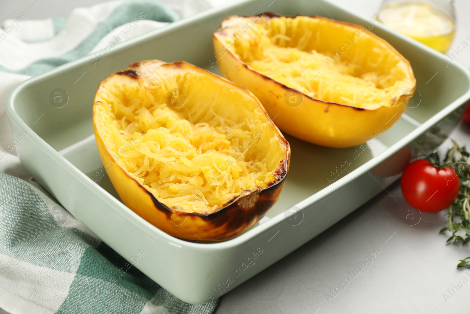 Photo of Halves of cooked spaghetti squash in baking dish on light grey table, closeup