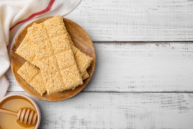 Board with tasty sesame kozinaki bars and honey on white wooden table, flat lay. Space for text