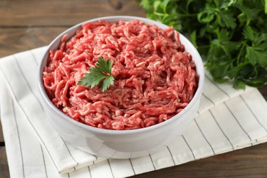 Raw ground meat in bowl and parsley on wooden table, closeup