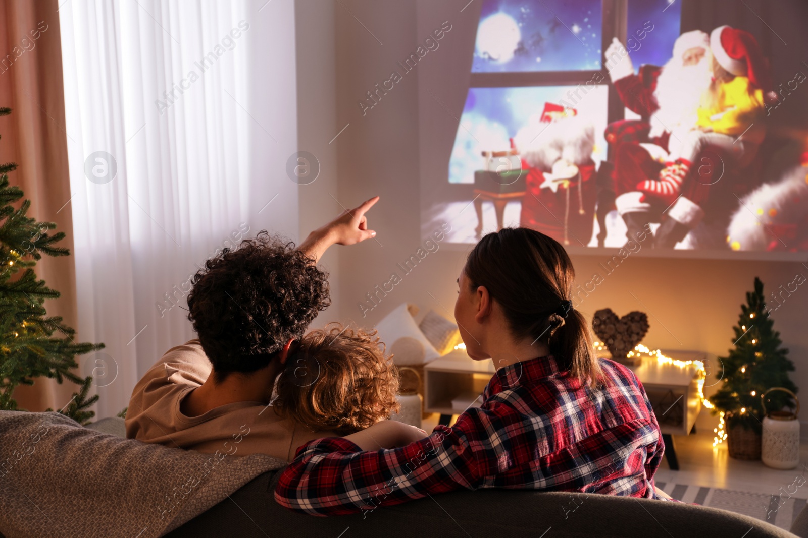 Photo of Family watching Christmas movie via video projector at home, back view