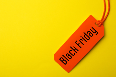 Image of Tag with phrase BLACK FRIDAY on yellow background, top view. Space for text