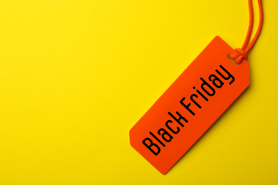 Tag with phrase BLACK FRIDAY on yellow background, top view. Space for text