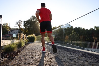 Photo of Man running outdoors on sunny day, back view