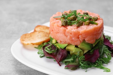 Tasty salmon tartare with avocado, greens and croutons on grey table, closeup