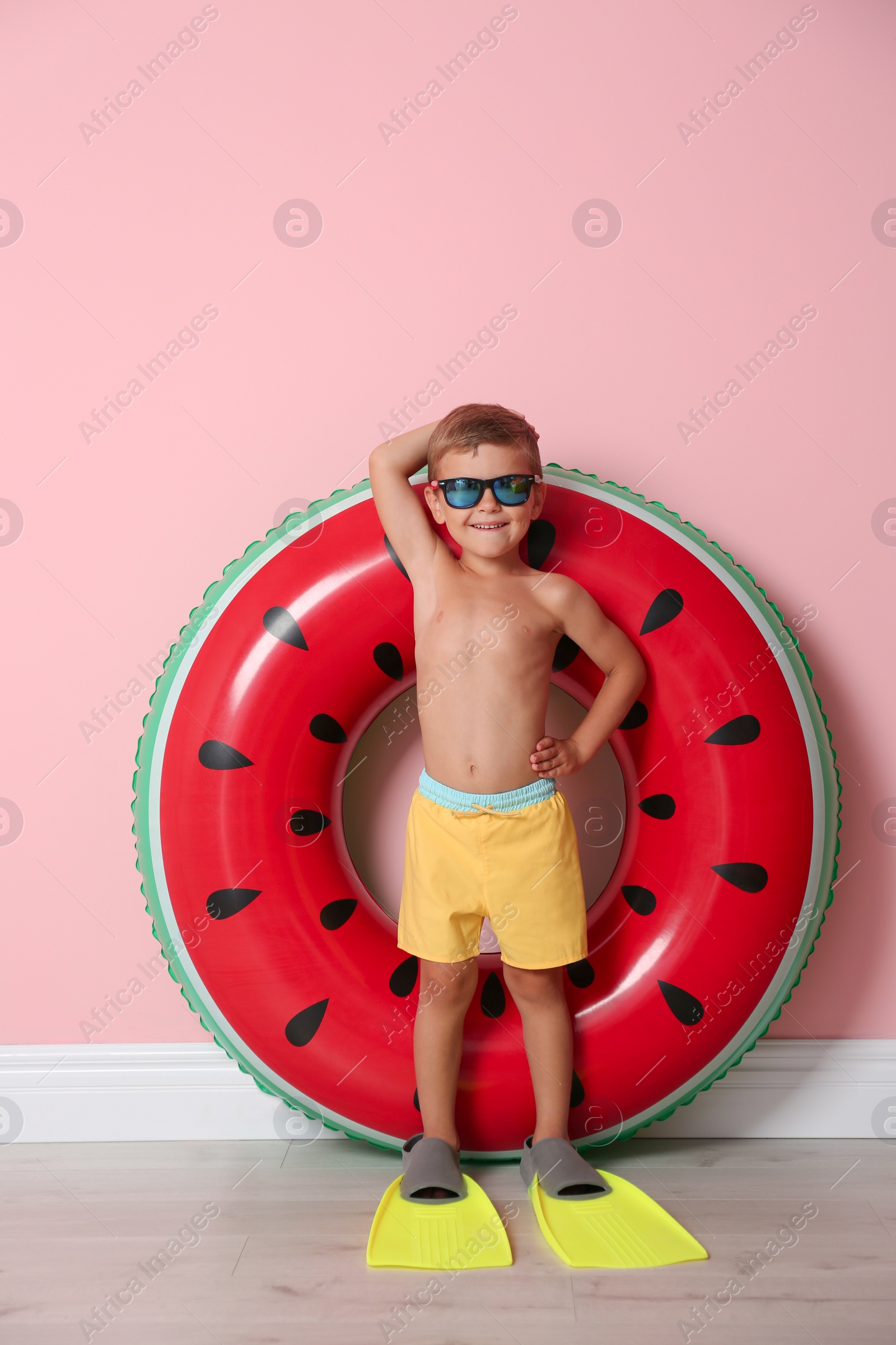 Photo of Cute little boy with inflatable ring wearing flippers near color wall