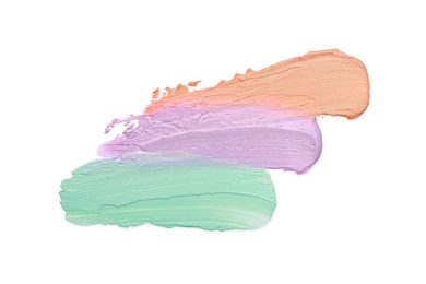 Strokes of pink, green and purple color correcting concealers on white background, top view