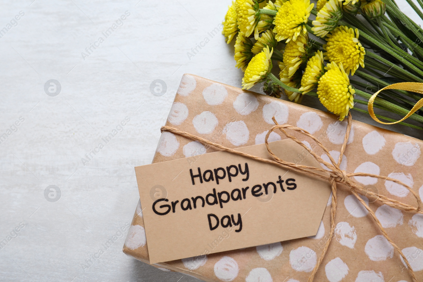 Photo of Beautiful yellow flowers, gift box and tag with phrase Happy Grandparents Day on light background, flat lay